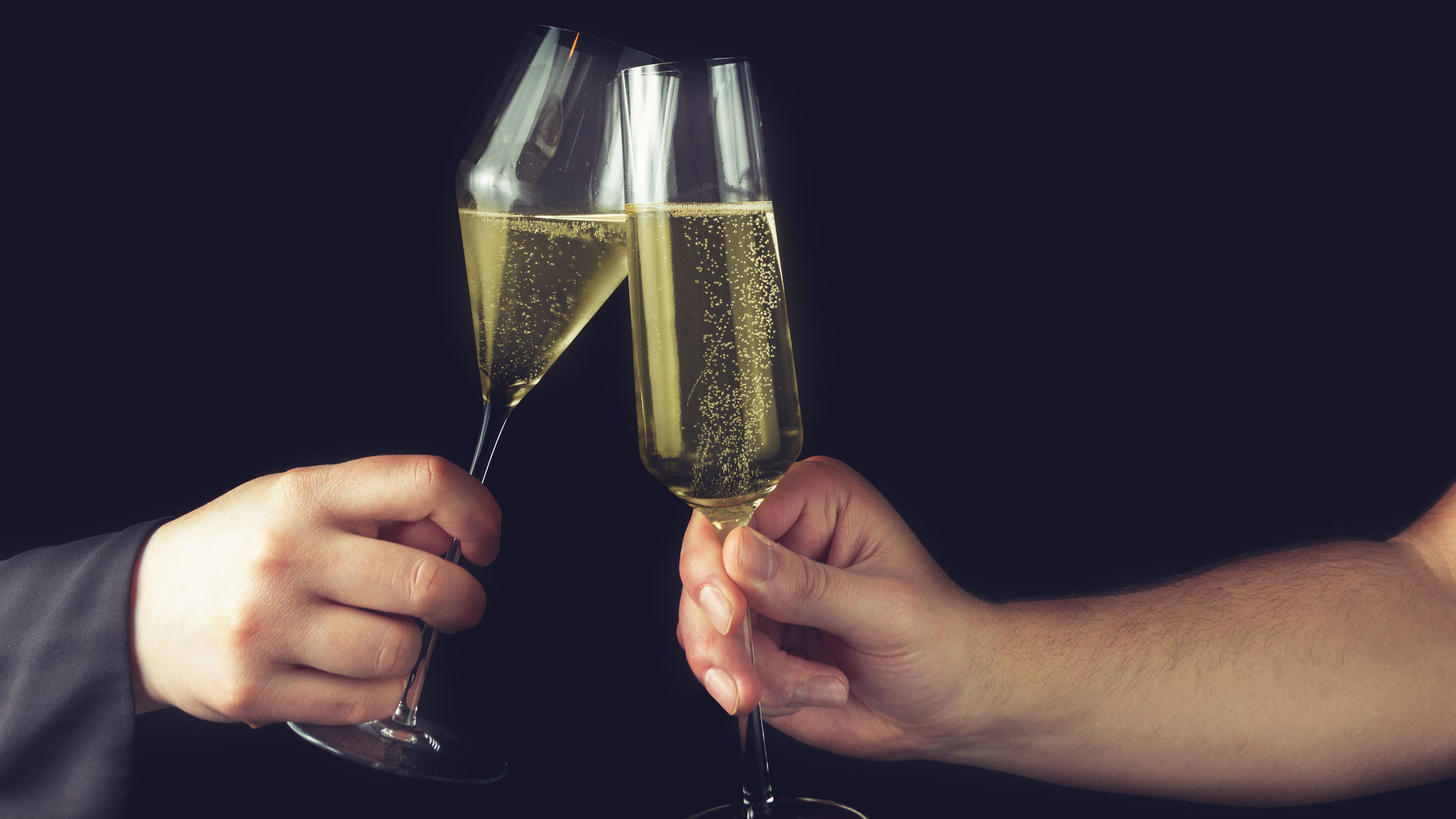 Couple clinking champagne glasses against a black background, capturing the glamour and celebration of sugar daddy roleplay